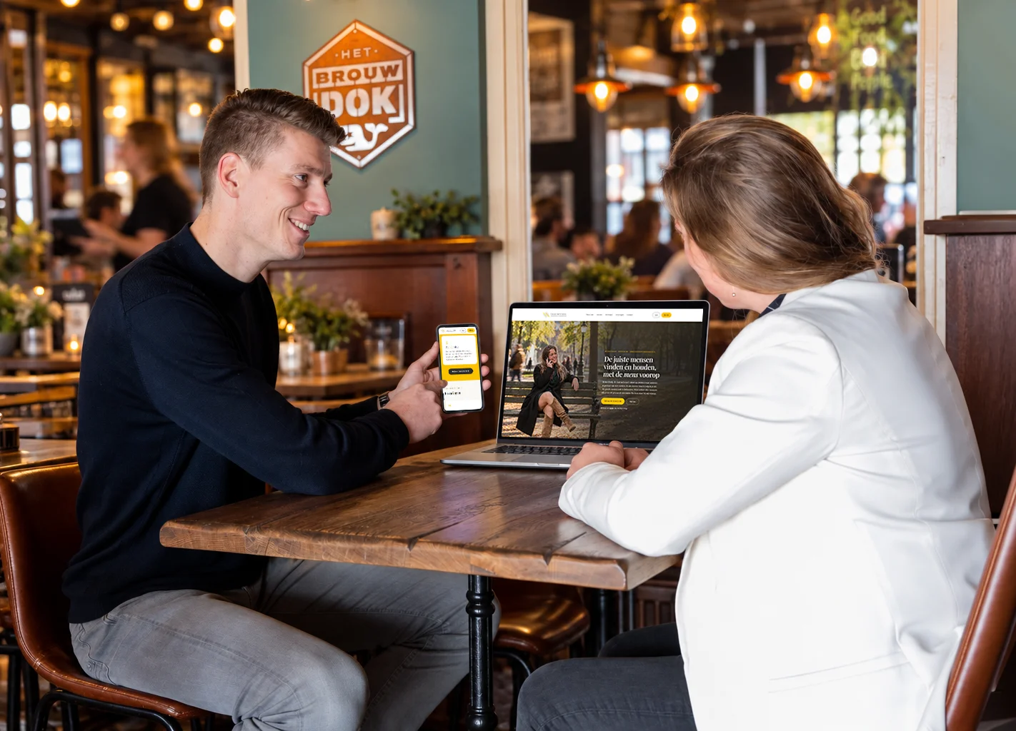Website Emily Mitchell op laptop en telefoon, besproken aan tafel in een café